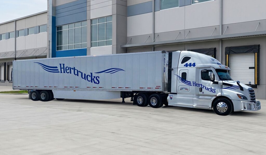 Una unidad de carga de Hertrucks permanece estacionada frente a un complejo logístico. La imagen muestra un tractocamión acoplado a una caja seca utilizada para el transporte de mercancías en rutas de distribución nacional.