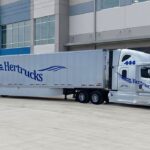 Tractocamión de Hertrucks con caja seca estacionado frente a un centro de distribución y logística.