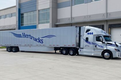 Tractocamión de Hertrucks con caja seca estacionado frente a un centro de distribución y logística.