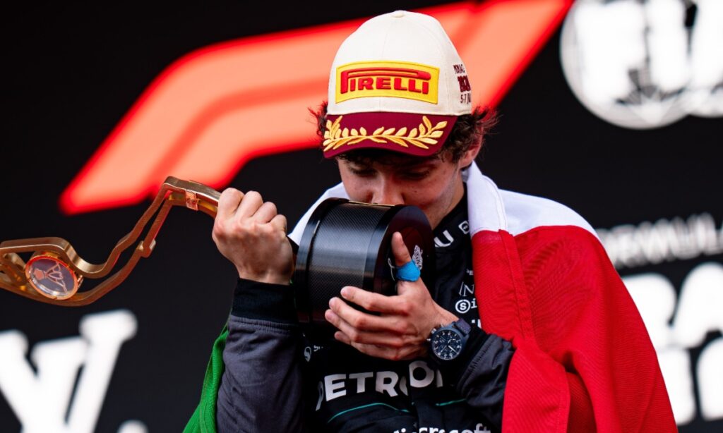 Kimi Antonelli besa un trofeo durante la ceremonia de podio mientras porta la bandera de México.