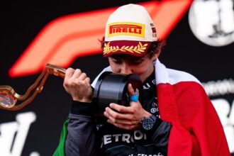Kimi Antonelli besa un trofeo durante la ceremonia de podio mientras porta la bandera de México.
