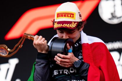 Kimi Antonelli besa un trofeo durante la ceremonia de podio mientras porta la bandera de México.