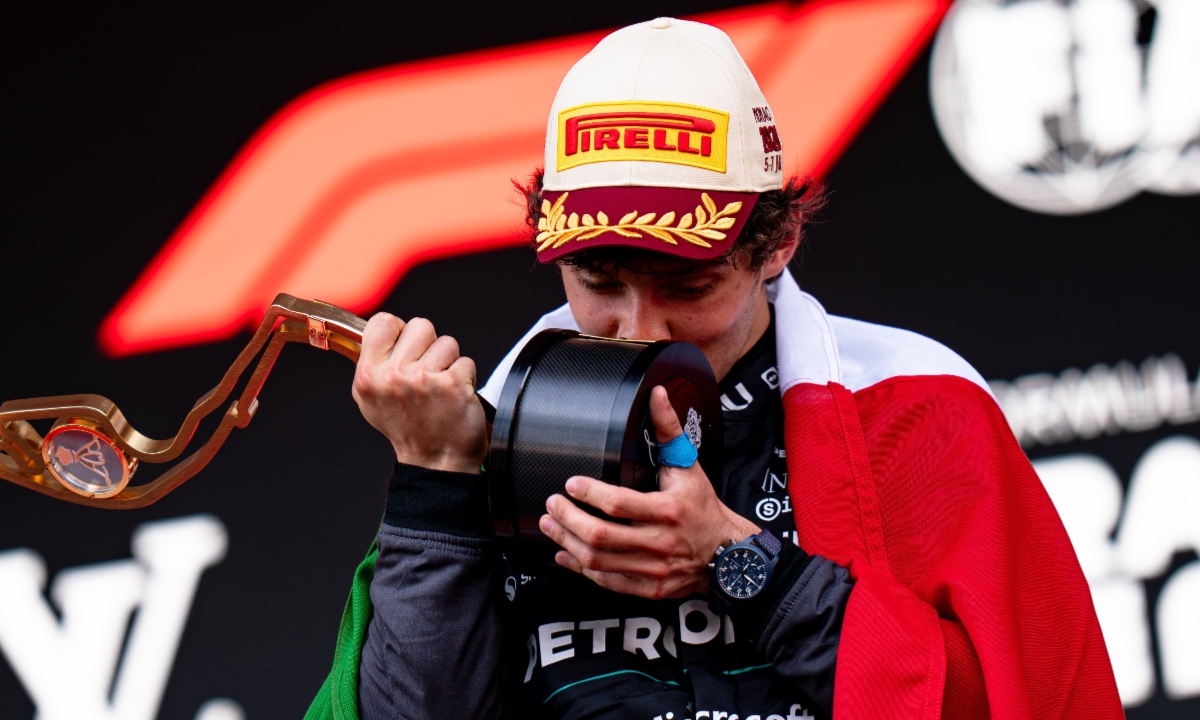 Kimi Antonelli besa un trofeo durante la ceremonia de podio mientras porta la bandera de México.