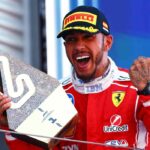 Lewis Hamilton celebra en el podio tras ganar el Gran Premio de Barcelona con Ferrari mientras sostiene el trofeo de ganador.