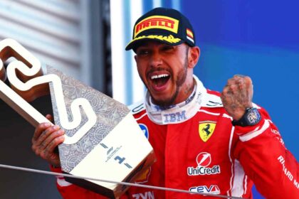 Lewis Hamilton celebra en el podio tras ganar el Gran Premio de Barcelona con Ferrari mientras sostiene el trofeo de ganador.