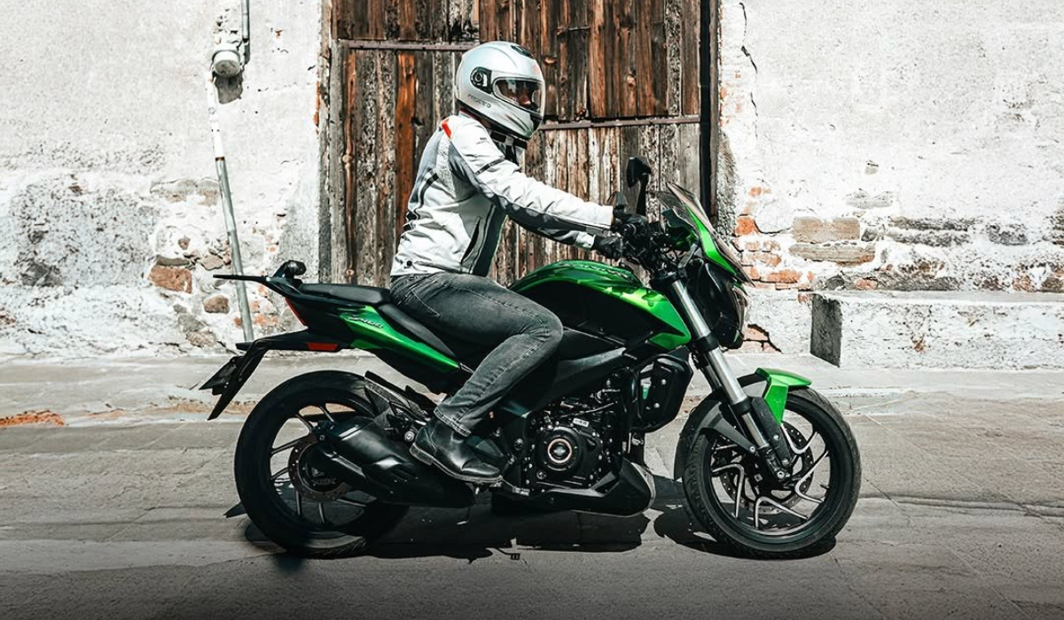 Motociclista con equipo de protección conduce una motocicleta de turismo urbano frente a una fachada tradicional de piedra y madera.