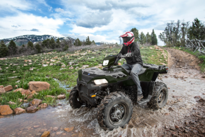 Vehículo todoterreno Polaris Sportsman 850 cruzando un arroyo en una ruta off road rodeada de montañas y vegetación natural.