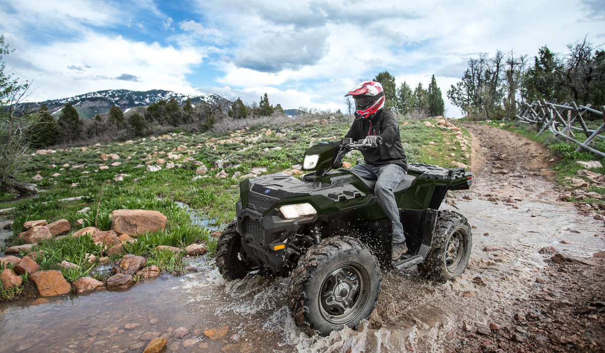 Vehículo todoterreno Polaris Sportsman 850 cruzando un arroyo en una ruta off road rodeada de montañas y vegetación natural.