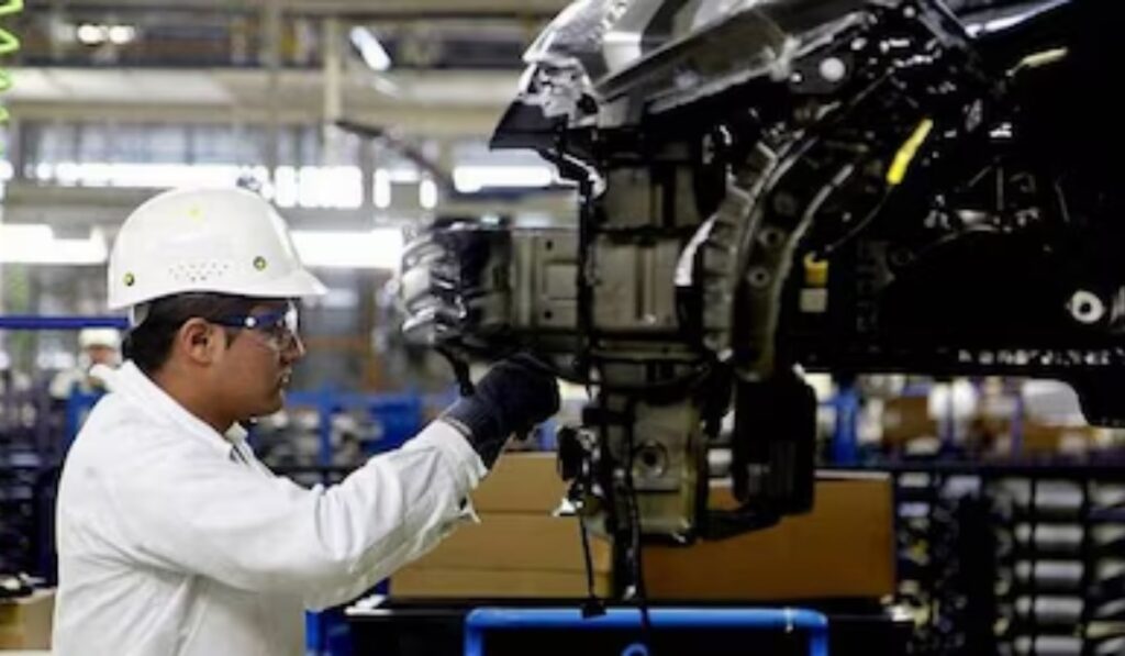 Trabajador con casco y equipo de seguridad inspecciona componentes de un vehículo en una línea de producción automotriz.