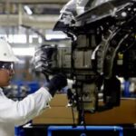 Trabajador con casco y equipo de seguridad inspecciona componentes de un vehículo en una línea de producción automotriz.