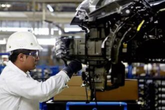 Trabajador con casco y equipo de seguridad inspecciona componentes de un vehículo en una línea de producción automotriz.