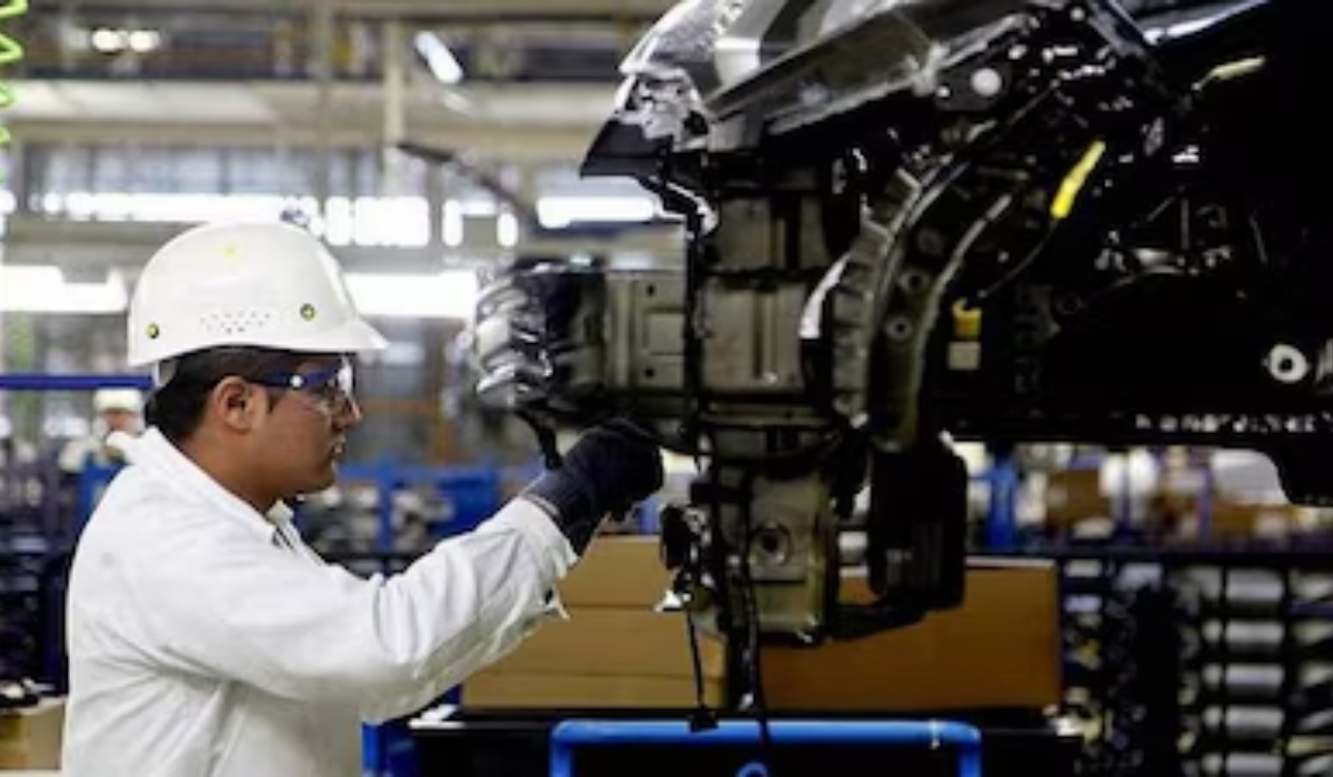 Trabajador con casco y equipo de seguridad inspecciona componentes de un vehículo en una línea de producción automotriz.