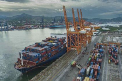 Buque portacontenedores atracado en una terminal del Puerto de Manzanillo junto a grúas pórtico y patios de almacenamiento de contenedores.