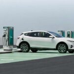 Vehículo eléctrico blanco conectado a una estación de carga rápida en un hub de recarga de VEMO con múltiples cargadores disponibles.