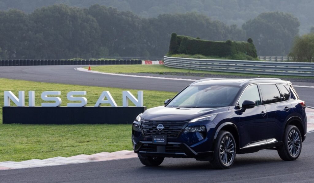 SUV Nissan X-Trail e-POWER con tecnología e-4ORCE en color azul oscuro estacionada en un circuito de carreras frente a letras tridimensionales de Nissan.