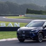 SUV Nissan X-Trail e-POWER con tecnología e-4ORCE en color azul oscuro estacionada en un circuito de carreras frente a letras tridimensionales de Nissan.