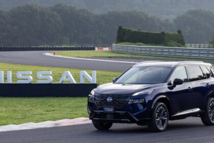 SUV Nissan X-Trail e-POWER con tecnología e-4ORCE en color azul oscuro estacionada en un circuito de carreras frente a letras tridimensionales de Nissan.