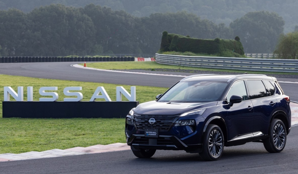 SUV Nissan X-Trail e-POWER con tecnología e-4ORCE en color azul oscuro estacionada en un circuito de carreras frente a letras tridimensionales de Nissan.