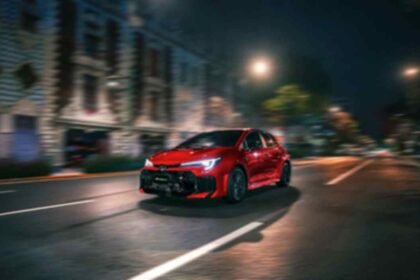 Toyota GR Corolla 2026 en color rojo circula de noche por una avenida urbana, destacando su diseño deportivo y tecnología desarrollada por GAZOO Racing.