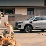 Una familia de cuatro integrantes con un perro Golden Retriever conviviendo frente a una SUV Chirey Tiggo PHEV de color blanco conectada a una estación de carga en casa.