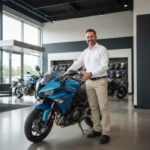 Hombre posando sonriente junto a una moto deportiva azul en una agencia de ventas, ilustrando los consejos para elegir la primera motocicleta.