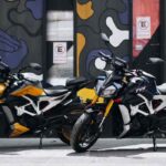 Dos motocicletas deportivas TVS Apache RTR 310 en colores amarillo y azul estacionadas frente a un mural urbano.