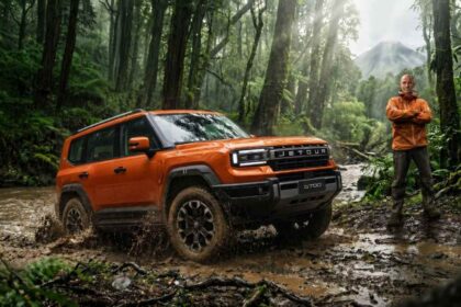 El explorador británico Ed Stafford junto a un JETOUR G700 de color naranja sobre un camino de lodo en la selva ecuatoriana, con el volcán Reventador al fondo.