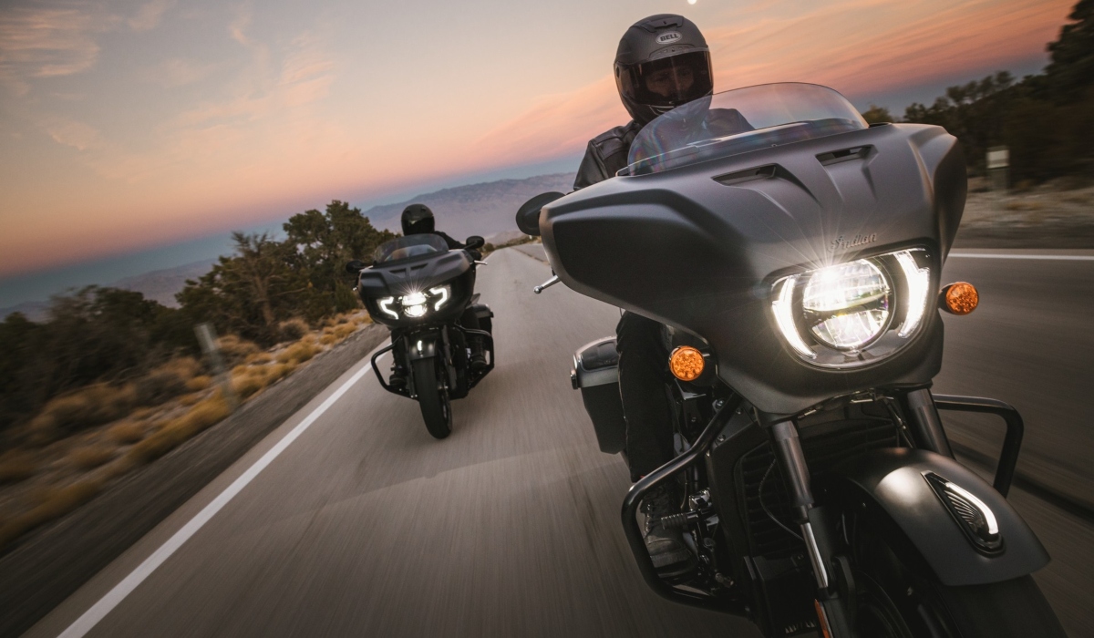 Dos motocicletas Indian tipo bagger navegando en carretera al atardecer equipadas con sistemas de seguridad inteligente SmartLean y cascos de protección.