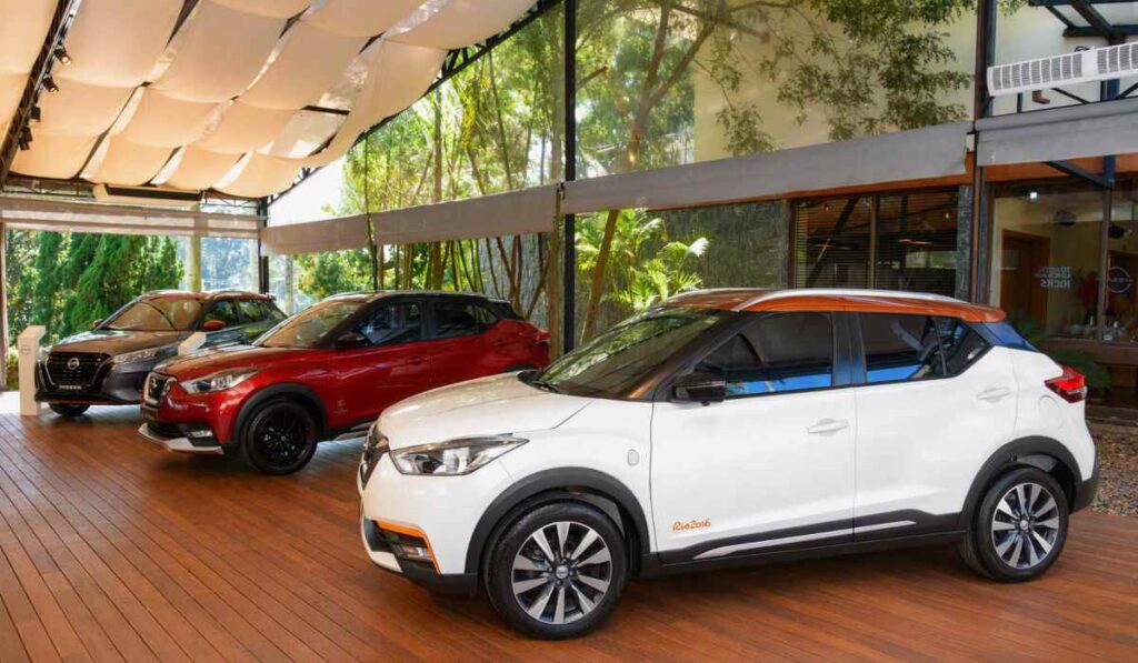 Tres generaciones y ediciones especiales de Nissan Kicks exhibidas en una sala, destacando el modelo blanco Rio 2016 con techo naranja en primer plano.
