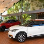 Tres generaciones y ediciones especiales de Nissan Kicks exhibidas en una sala, destacando el modelo blanco Rio 2016 con techo naranja en primer plano.