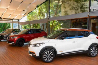 Tres generaciones y ediciones especiales de Nissan Kicks exhibidas en una sala, destacando el modelo blanco Rio 2016 con techo naranja en primer plano.