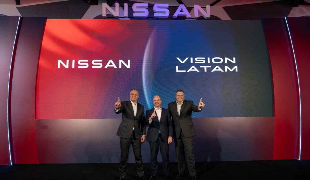 Tres ejecutivos de Nissan en el escenario apuntando hacia arriba frente a una pantalla con la inscripción Nissan Vision Latam.