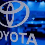 Logotipo corporativo de Toyota iluminado en azul con la silueta de un vehiculo desenfocada al fondo, representando la estrategia financiera y de movilidad de la marca.