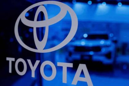 Logotipo corporativo de Toyota iluminado en azul con la silueta de un vehiculo desenfocada al fondo, representando la estrategia financiera y de movilidad de la marca.