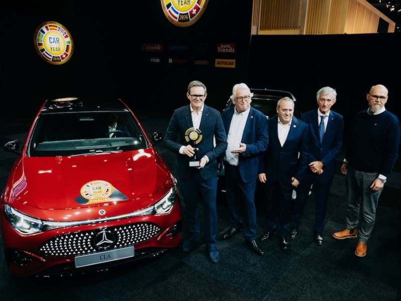 Ejecutivos de Mercedes-Benz sosteniendo el premio Car of the Year 2026 junto al nuevo Mercedes-Benz CLA color rojo en el Salón del Automóvil de Bruselas.
