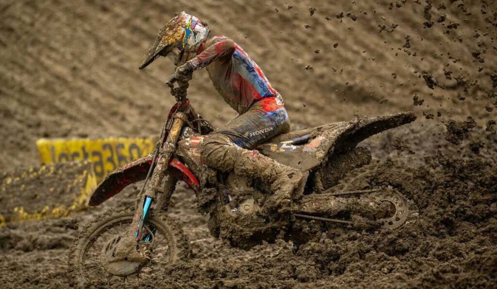 Piloto de Honda HRC Progressive maniobrando su motocicleta cubierta de lodo en una pista extrema del Campeonato SMX en Columbus, Ohio.