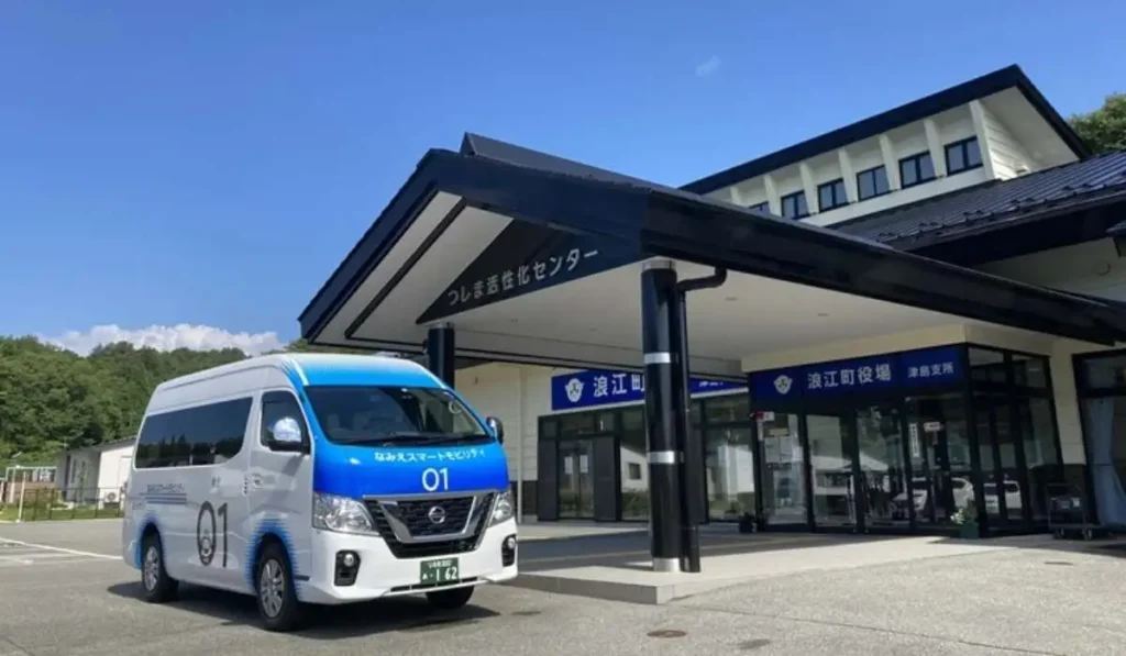Minibús blanco y azul del programa Namie Smart Mobility de Nissan estacionado frente a un edificio público en Japón.