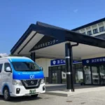 Minibús blanco y azul del programa Namie Smart Mobility de Nissan estacionado frente a un edificio público en Japón.