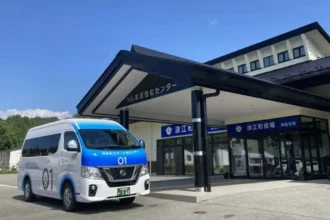 Minibús blanco y azul del programa Namie Smart Mobility de Nissan estacionado frente a un edificio público en Japón.