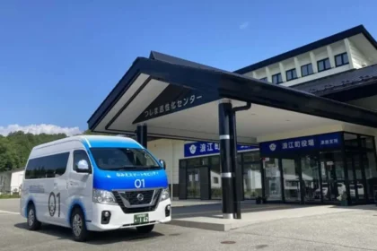 Minibús blanco y azul del programa Namie Smart Mobility de Nissan estacionado frente a un edificio público en Japón.