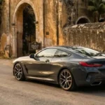 Automóvil deportivo de lujo color gris circulando por un camino pavimentado frente a una histórica hacienda en la Península de Yucatán.