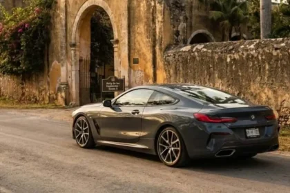 Automóvil deportivo de lujo color gris circulando por un camino pavimentado frente a una histórica hacienda en la Península de Yucatán.