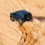 SUV todoterreno de color oscuro levantando arena mientras circula por las dunas del desierto del Sahara durante la expedición de Ed Stafford.