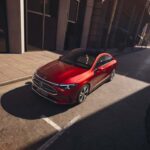 Vista superior del nuevo Mercedes-Benz CLA eléctrico color rojo estacionado en una calle urbana iluminada por el sol.