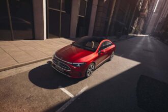 Vista superior del nuevo Mercedes-Benz CLA eléctrico color rojo estacionado en una calle urbana iluminada por el sol.