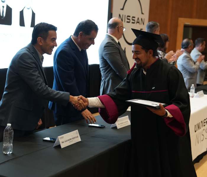 Egresado de la Universidad Nissan vistiendo toga y birrete estrechando la mano de un directivo al recibir su diploma en el presídium.