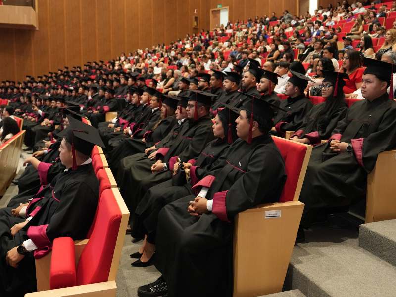 Estudiantes de la Universidad Nissan vistiendo toga y birrete sentados en las butacas de un auditorio durante la ceremonia de graduación.