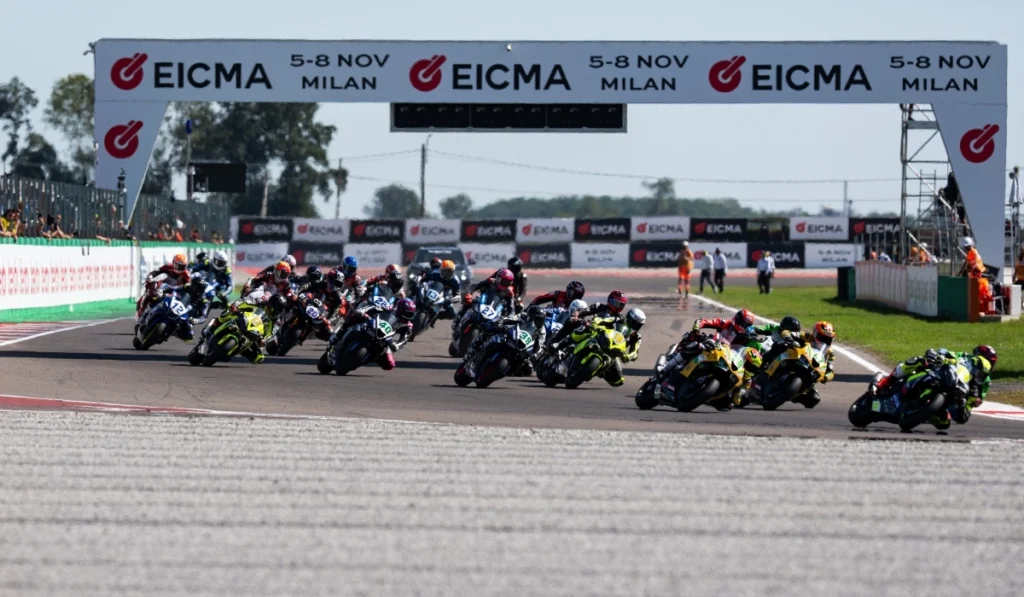 Grupo de motociclistas compitiendo en la pista bajo un arco publicitario del campeonato WorldSBK en el Circuito de Cremona.