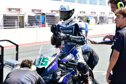 Piloto de ITALIKA Racing con indumentaria azul y blanca ajustando su postura sobre la motocicleta en el pit lane junto al equipo técnico.