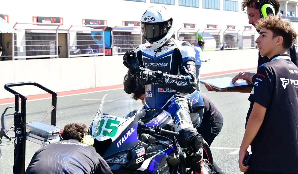 Piloto de ITALIKA Racing con indumentaria azul y blanca ajustando su postura sobre la motocicleta en el pit lane junto al equipo técnico.